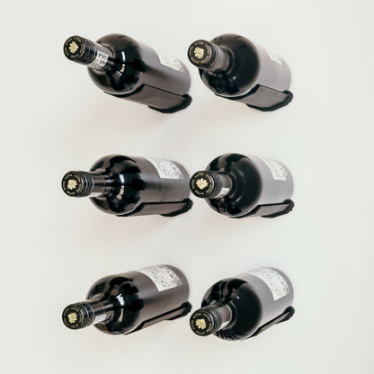 Six wine bottles on individual or solo pins that are wall mounted.