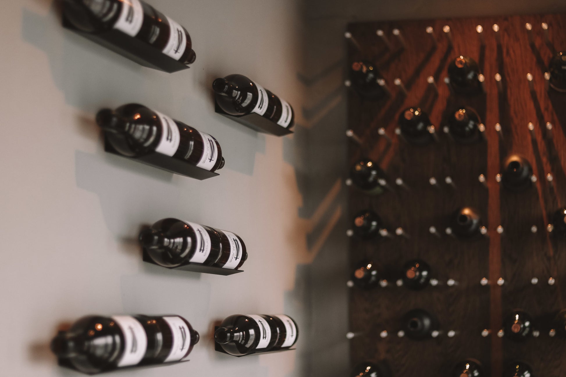 Wine bottles arranged on a wall-mounted rack with a wooden panel in the background.