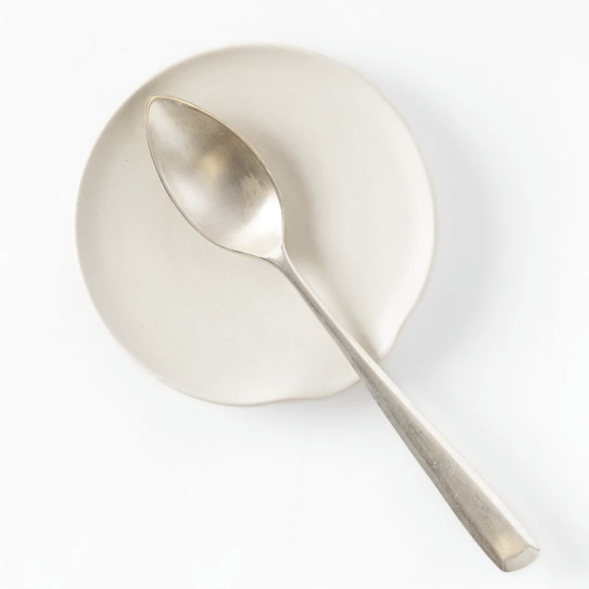 Silver spoon on a ceramic dish and set against a white background