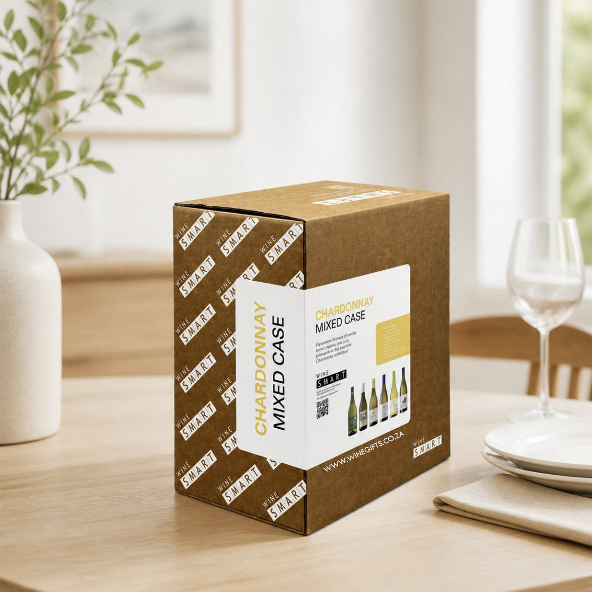 Wine box labeled 'Chardonnay Mixed Case' on a table with a glass and plates in the background