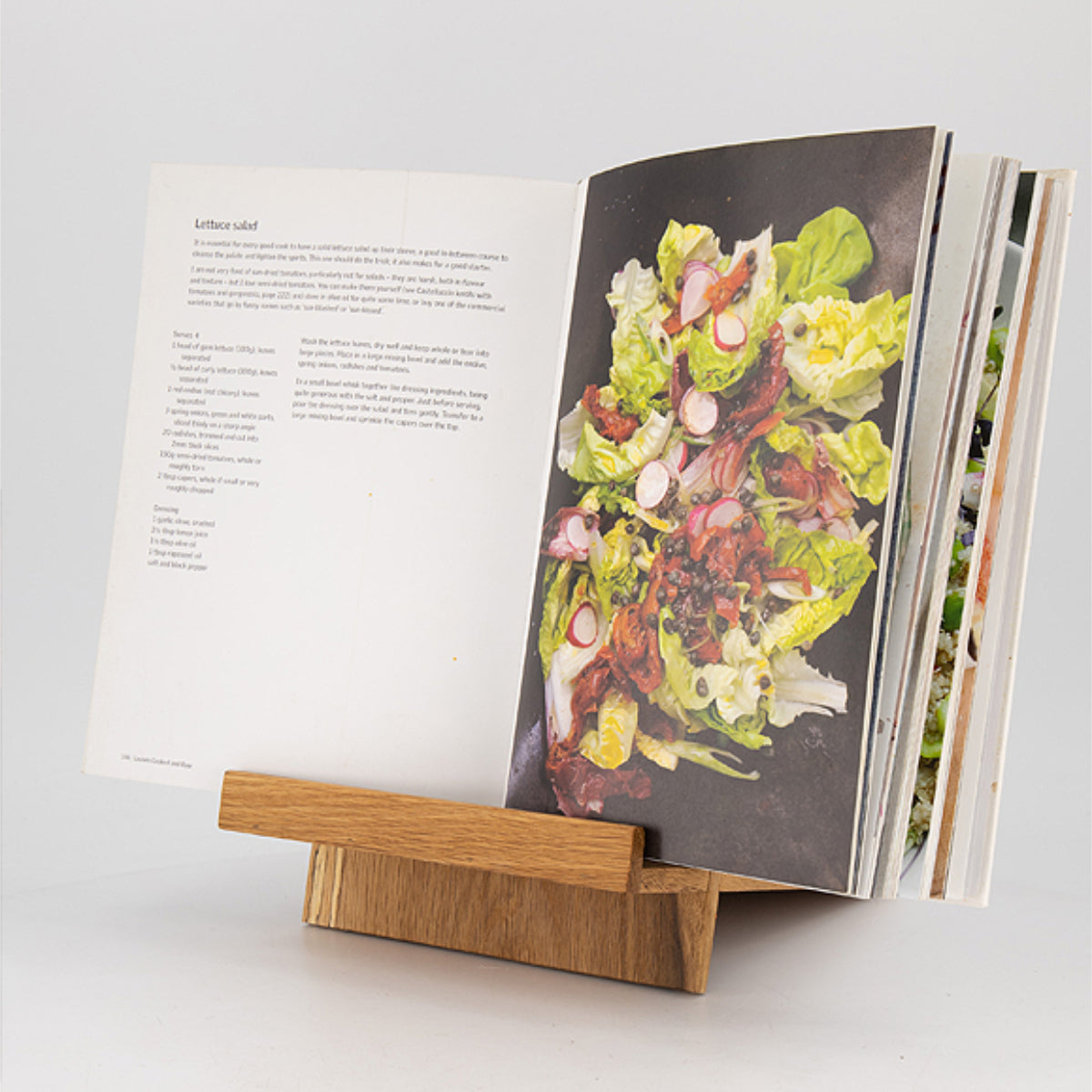 Wooden book stand holding an open cookbook with a salad image on a white background
