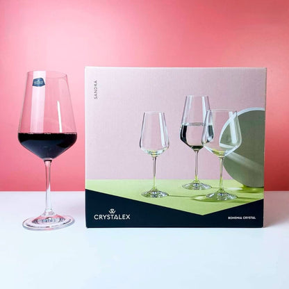 Wine glass with red wine next to a Crystalex packaging box on a pink background