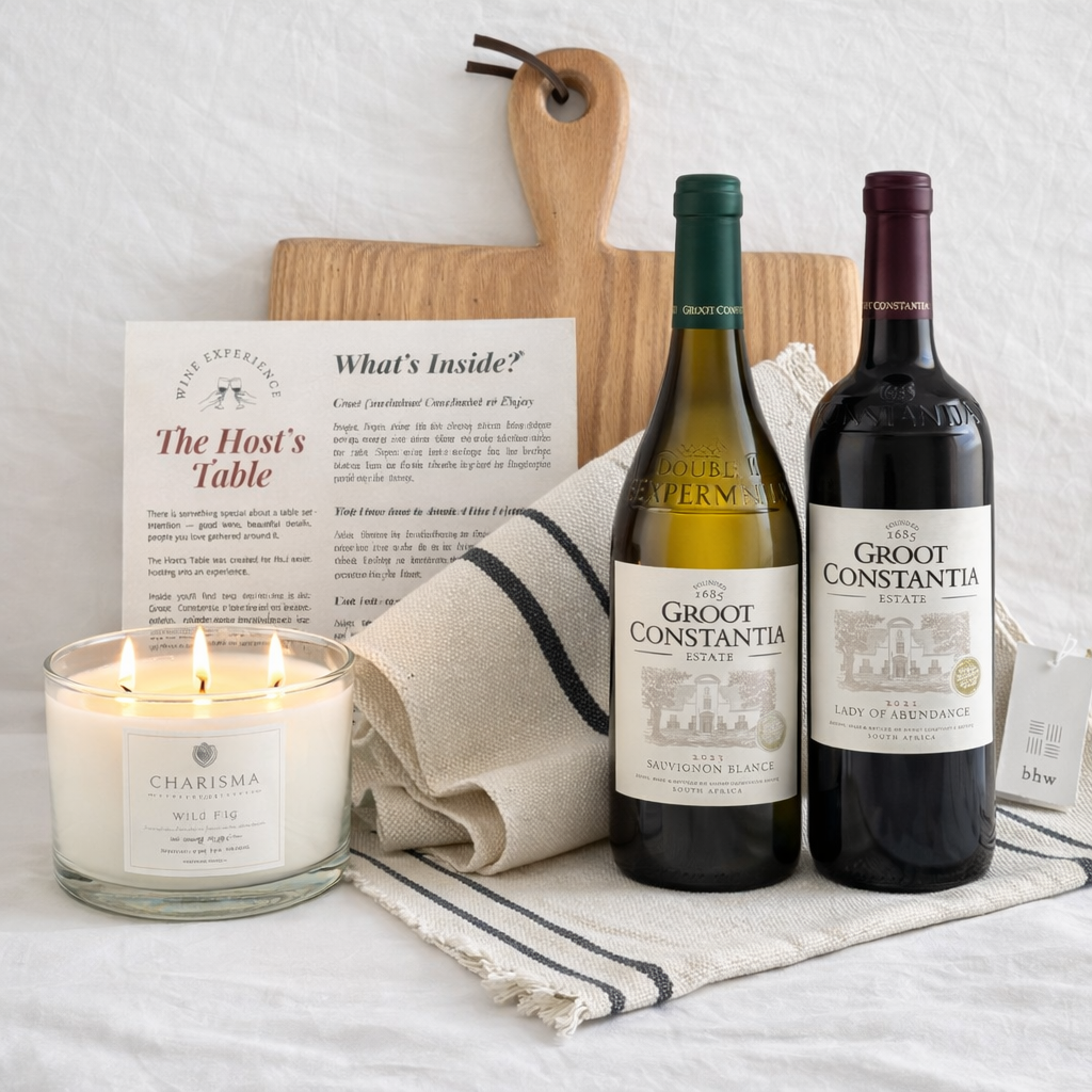 Two bottles of Groot Constantia wine, a lit candle, and a wooden cutting board on a white surface.
